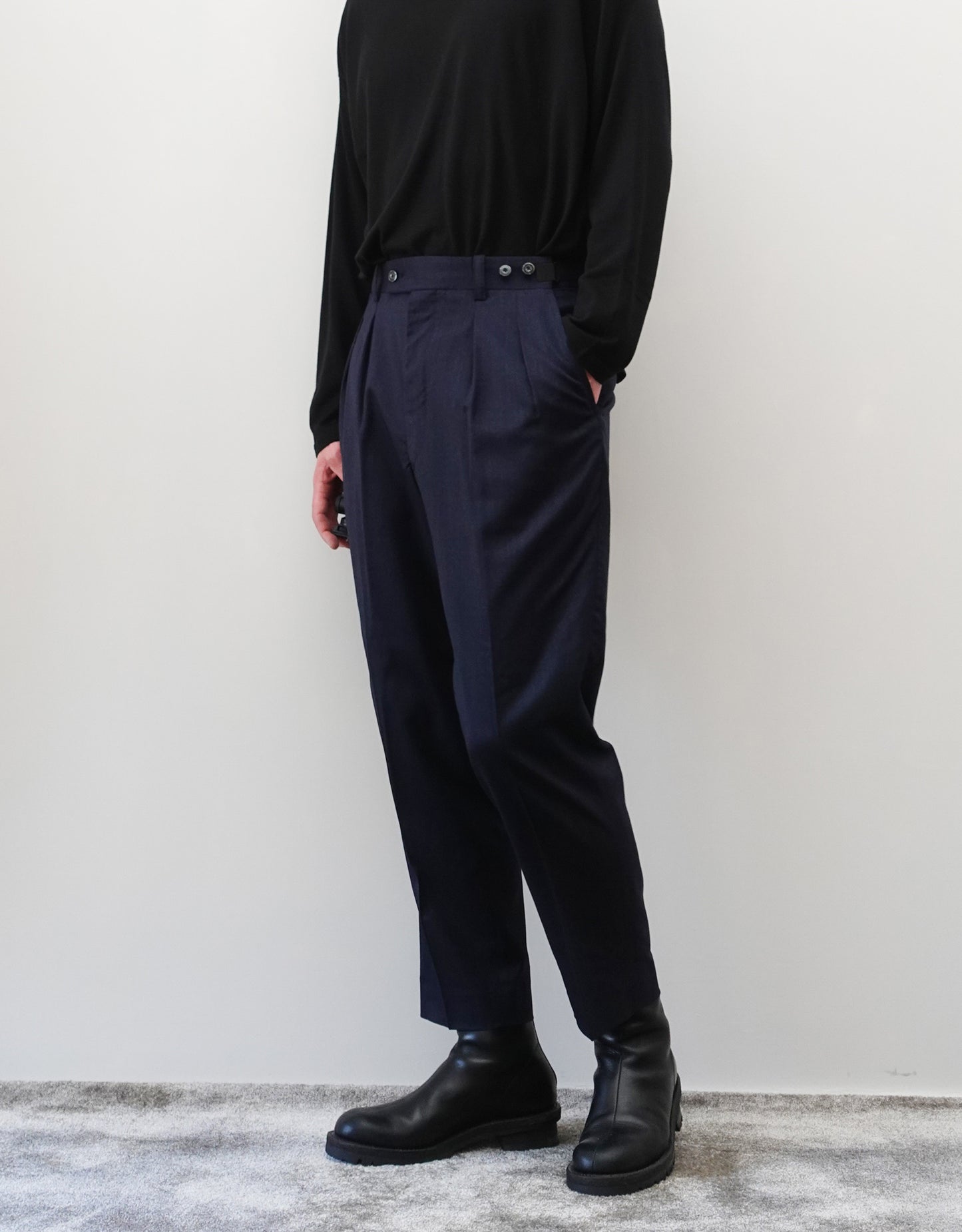 VOUILLON（ヴイヨン）のSuspender Two Tuck Trousers - Navy（サスペンダーツータックトラウザーズ）。ネイビーのツータックワイドパンツに、取り外し可能な同素材のサスペンダーを備えたディテール。サスペンダーを取り外したモデル着用画像。