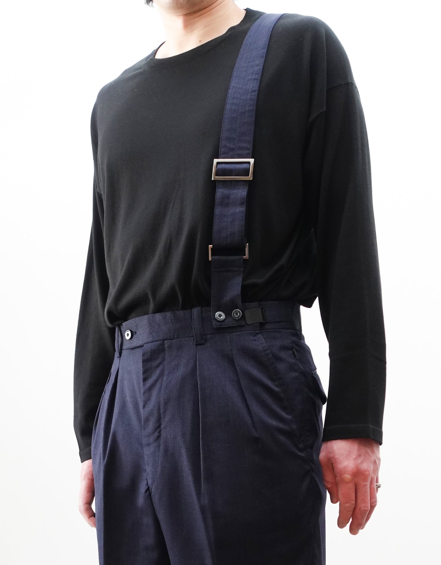 VOUILLON（ヴイヨン）のSuspender Two Tuck Trousers - Navy（サスペンダーツータックトラウザーズ）。ネイビーのツータックワイドパンツに、取り外し可能な同素材のサスペンダーを備えたディテール。モデル着用正面でサスペンダーのアップ画像。