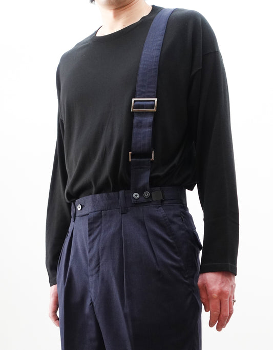 VOUILLON（ヴイヨン）のSuspender Two Tuck Trousers - Navy（サスペンダーツータックトラウザーズ）。ネイビーのツータックワイドパンツに、取り外し可能な同素材のサスペンダーを備えたディテール。モデル着用正面でサスペンダーのアップ画像。