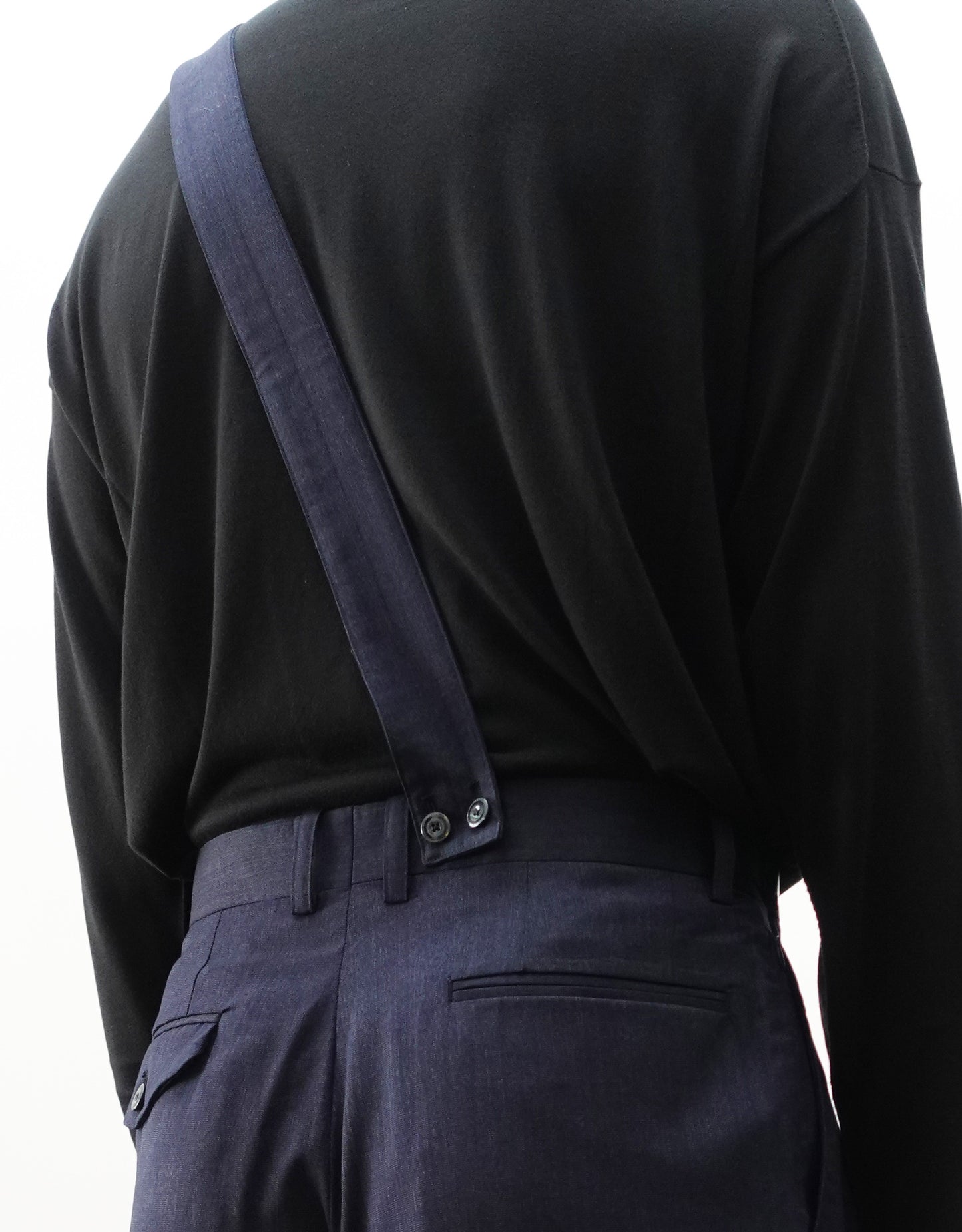 VOUILLON（ヴイヨン）のSuspender Two Tuck Trousers - Navy（サスペンダーツータックトラウザーズ）。ネイビーのツータックワイドパンツに、取り外し可能な同素材のサスペンダーを備えたディテール。モデル着用背面でサスペンダーのアップの画像。