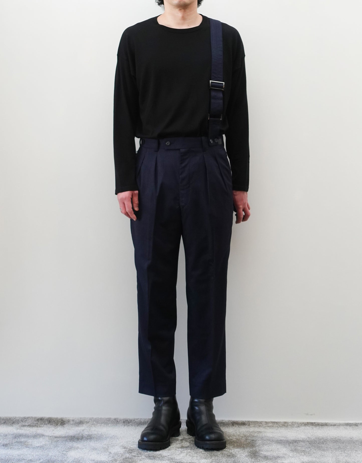 VOUILLON（ヴイヨン）のSuspender Two Tuck Trousers - Navy（サスペンダーツータックトラウザーズ）。ネイビーのツータックワイドパンツに、取り外し可能な同素材のサスペンダーを備えたディテール。モデル着用正面全身画像。