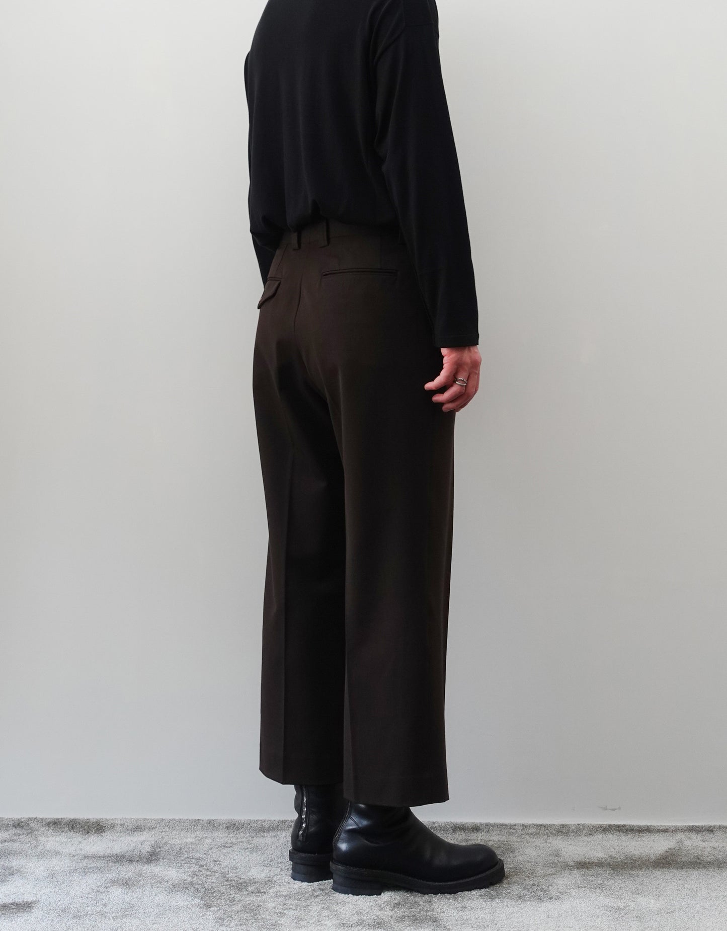 VOUILLON（ヴイヨン）のFour Pleats Wide Trousers - Dark Chocolate（4プリーツワイドトラウザーズ）。ダークチョコレート（深みのあるブラウン）のワイドシルエットと腰元の4プリーツ。モデルによる左斜め後向きの着用画像。