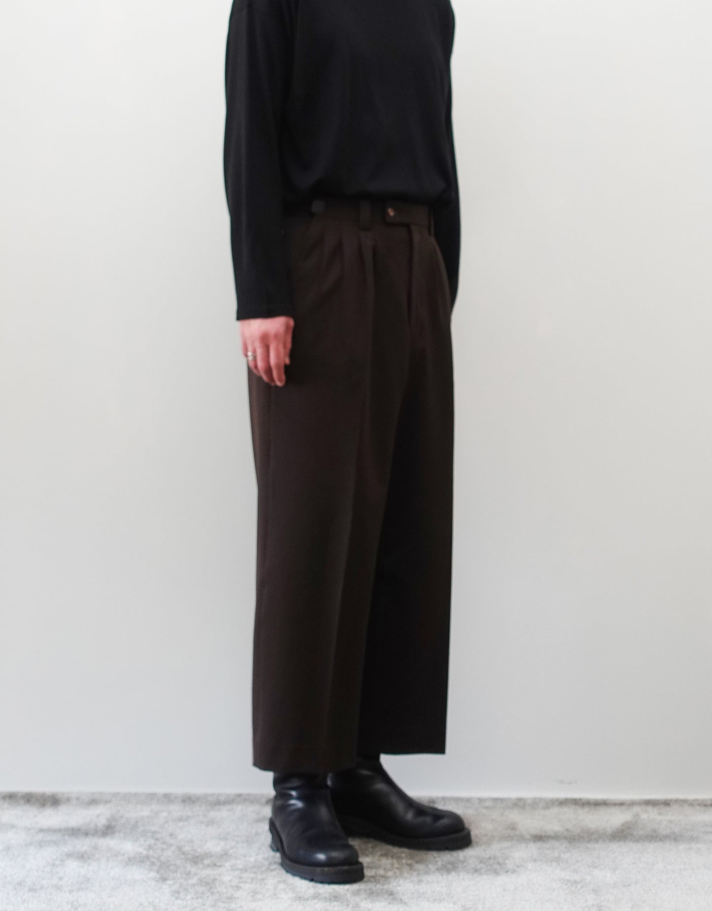 VOUILLON（ヴイヨン）のFour Pleats Wide Trousers - Dark Chocolate（4プリーツワイドトラウザーズ）。ダークチョコレート（深みのあるブラウン）のワイドシルエットと腰元の4プリーツ。モデルによる左斜め前向きの着用画像。