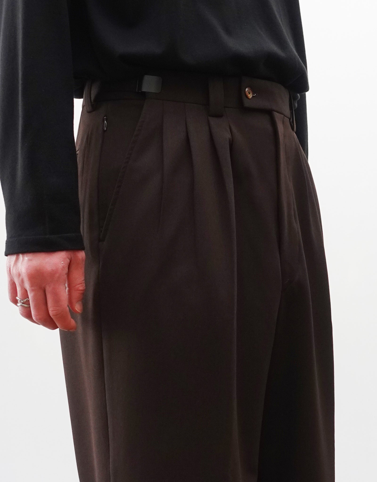 VOUILLON（ヴイヨン）のFour Pleats Wide Trousers - Dark Chocolate（4プリーツワイドトラウザーズ）。ダークチョコレート（深みのあるブラウン）のワイドシルエットと腰元の4プリーツ。モデルによる斜め左向きの着用画像のウエストアップ。
