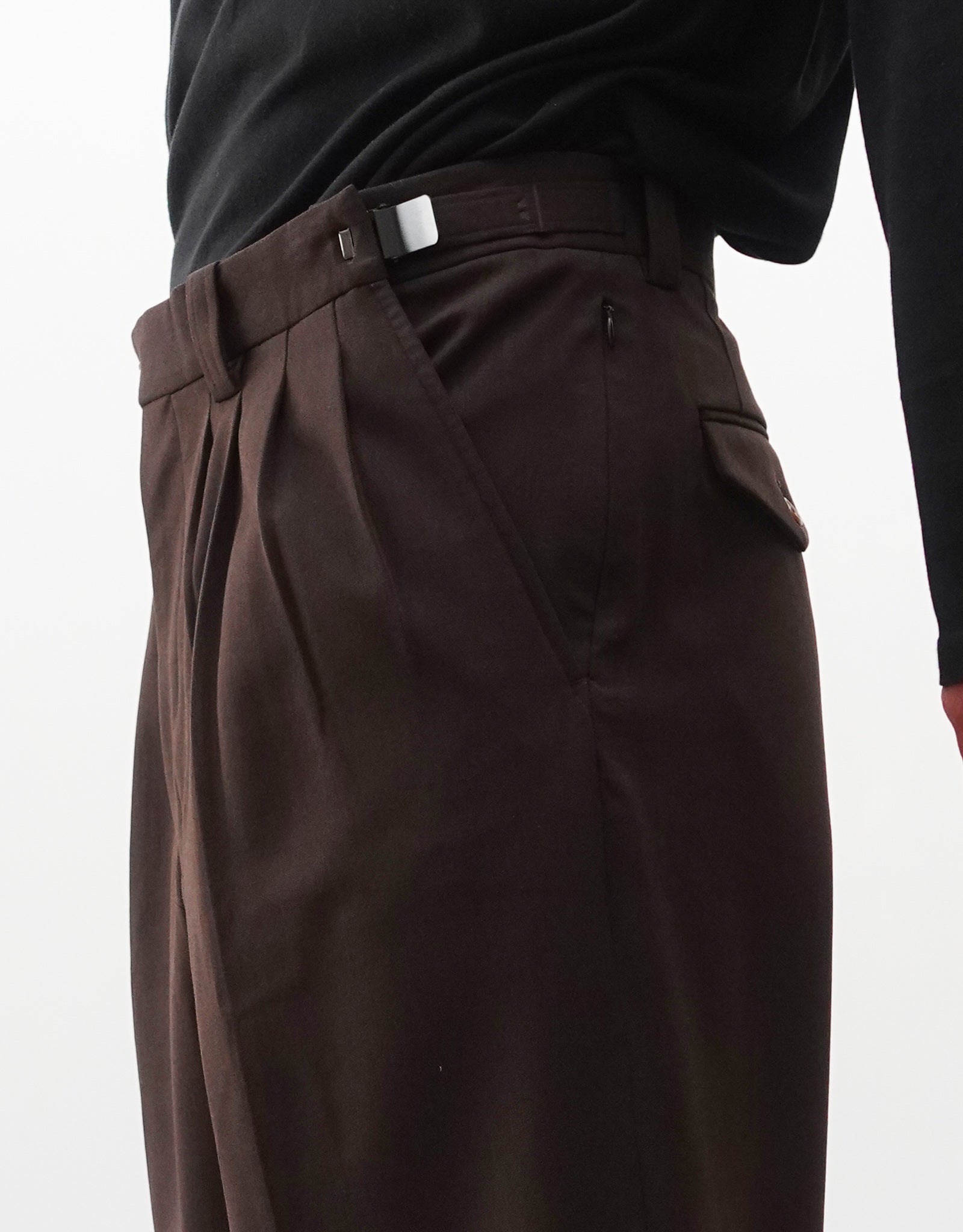 VOUILLON（ヴイヨン）のFour Pleats Wide Trousers - Dark Chocolate（4プリーツワイドトラウザーズ）。ダークチョコレート（深みのあるブラウン）のワイドシルエットと腰元の4プリーツ。モデルによる右斜め向きの着用のウエストアップとアジャスターベルトの説明画像。