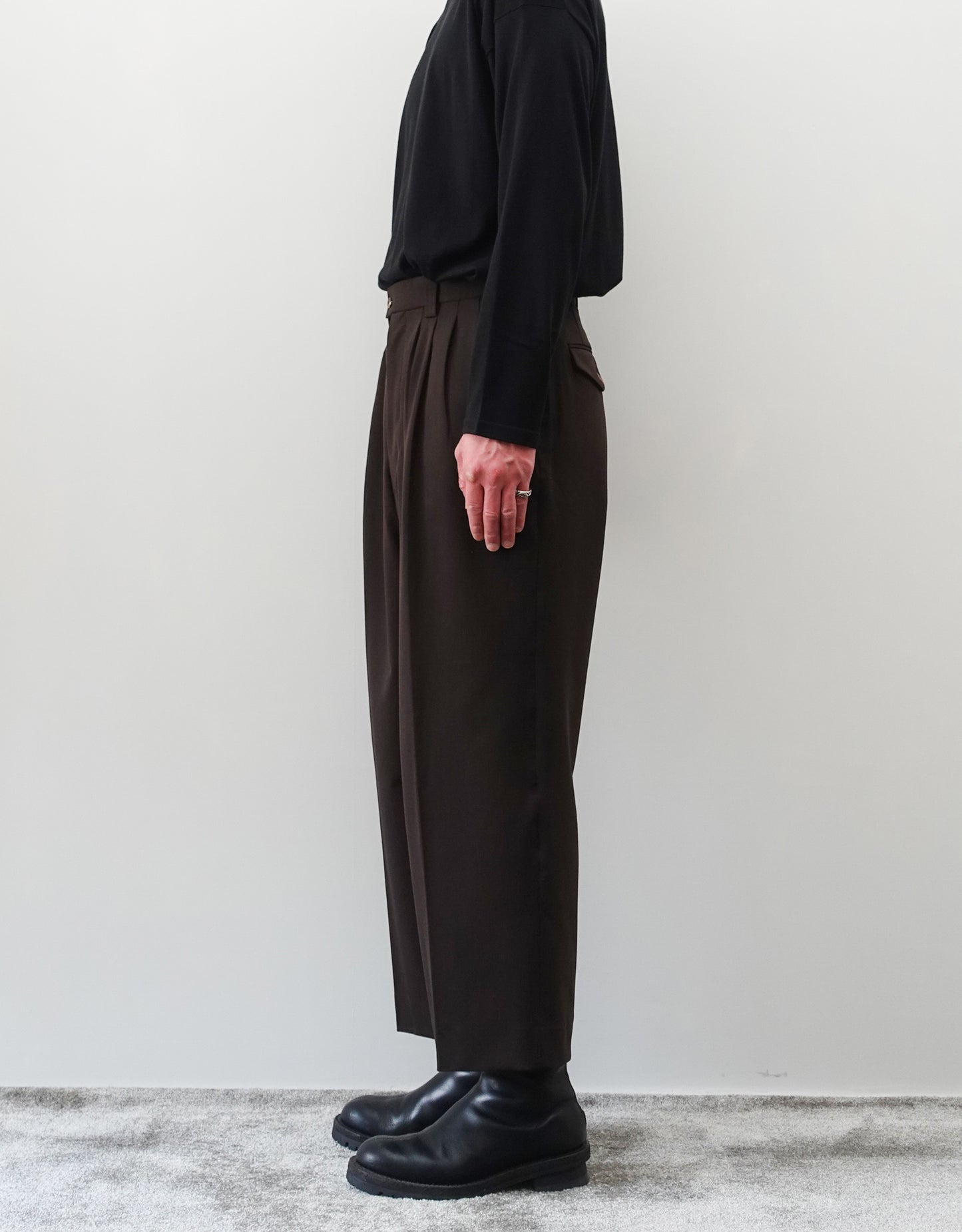 VOUILLON（ヴイヨン）のFour Pleats Wide Trousers - Dark Chocolate（4プリーツワイドトラウザーズ）。ダークチョコレート（深みのあるブラウン）のワイドシルエットと腰元の4プリーツ。モデルによる右向きの着用画像。