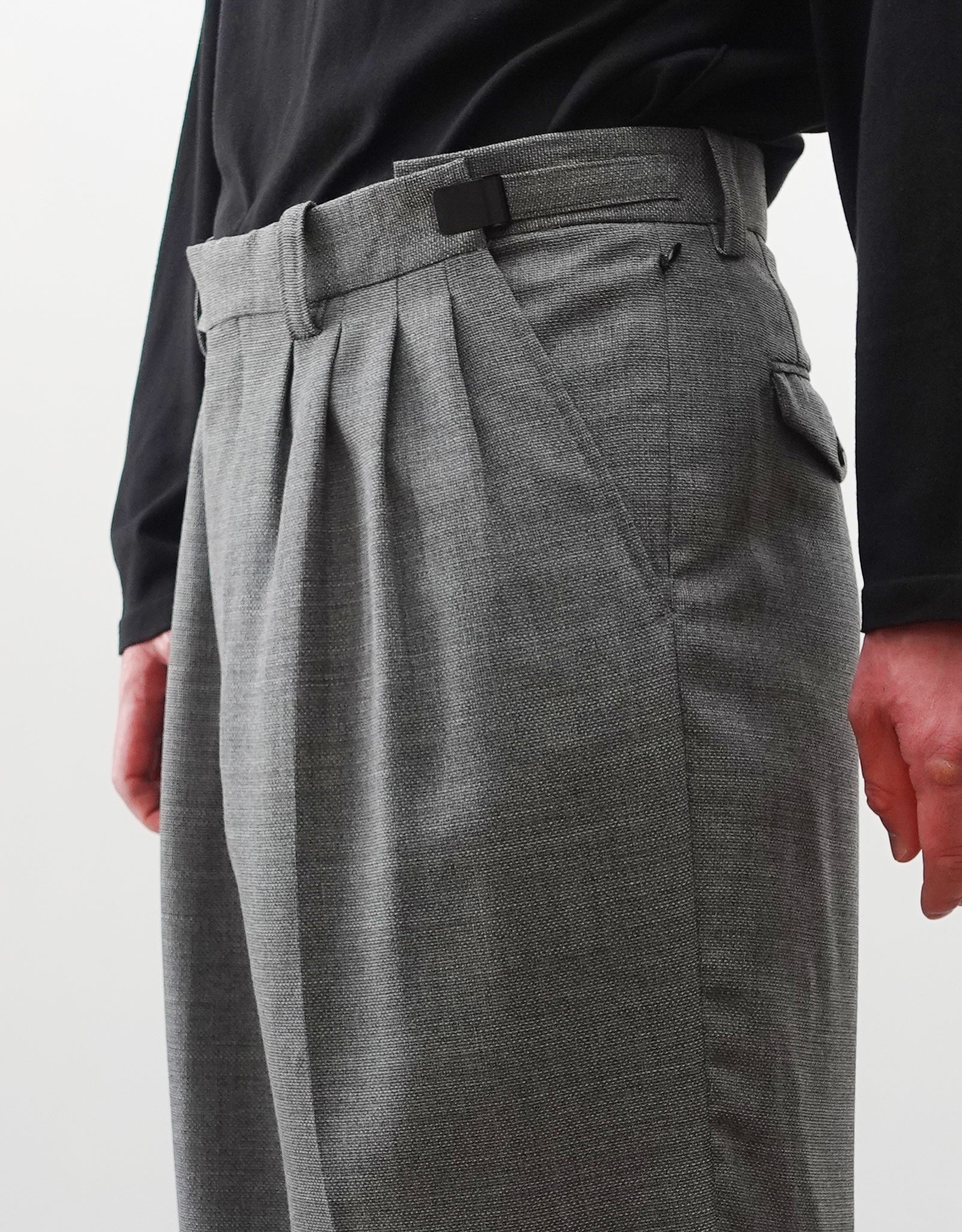 VOUILLON（ヴイヨン）のFour Pleats Wide Trousers - Gray（4プリーツワイドトラウザーズ）。ソリッドなグレーの生地に、腰元の4プリーツが深みのある陰影を生み出すワイドパンツ。洗練されたミニマルなスタイリング。モデル着用ウエストのアジャスターベルトの最大仕様の画像。