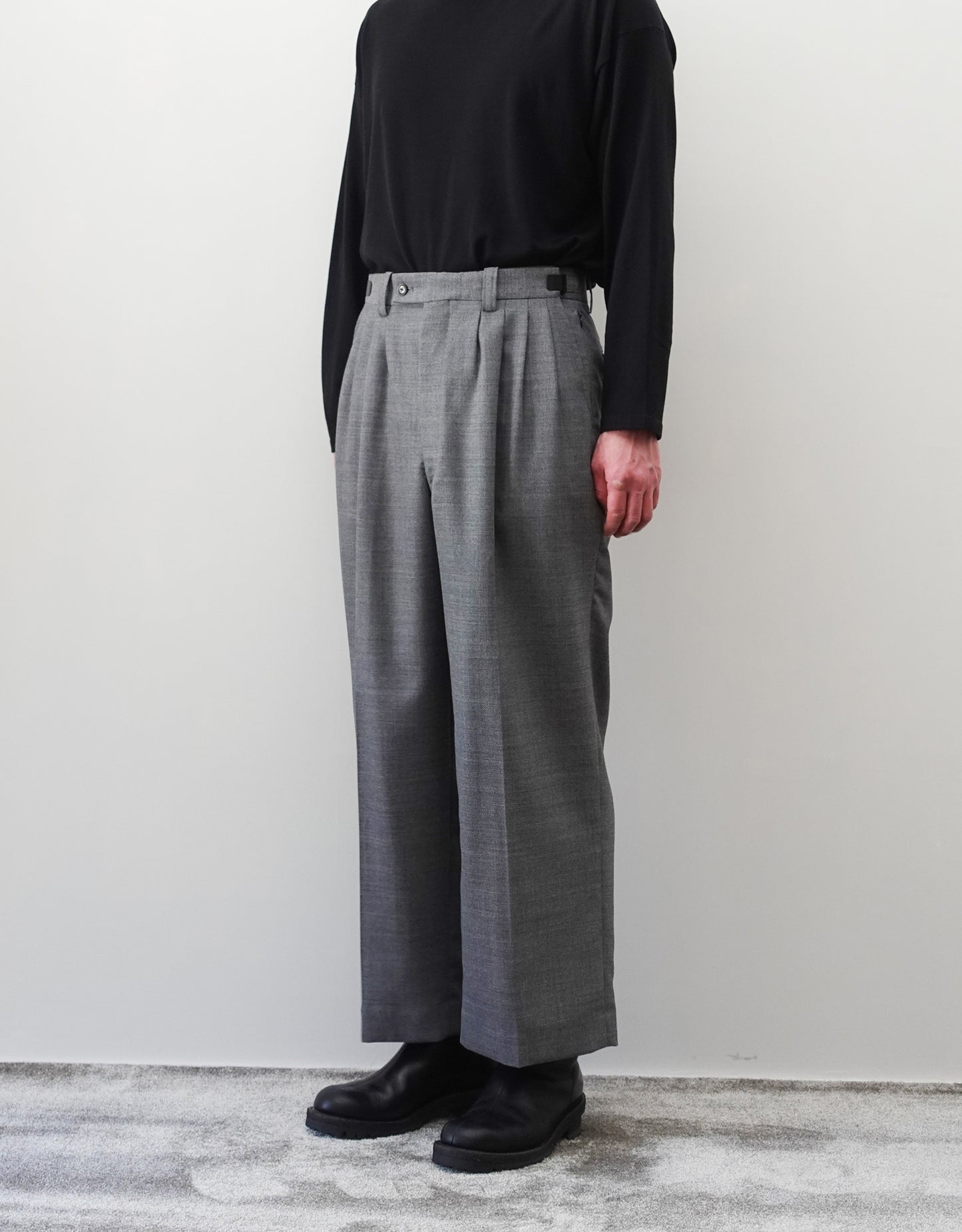 VOUILLON（ヴイヨン）のFour Pleats Wide Trousers - Gray（4プリーツワイドトラウザーズ）。ソリッドなグレーの生地に、腰元の4プリーツが深みのある陰影を生み出すワイドパンツ。洗練されたミニマルなスタイリング。モデル着用右斜め前向き画像。