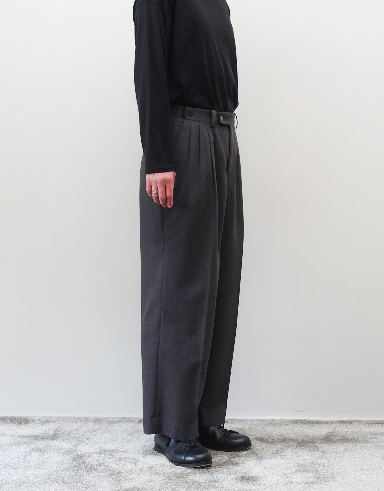 VOUILLON（ヴイヨン）のFour Pleats Wide Trousers - Gray Multi Stripe（4プリーツワイドトラウザーズ）。グレー地にマルチストライプを配した、4プリーツ仕様のワイドパンツ。ストライプによる脚長効果と立体的なシルエットが特徴。モデル着用左向き画像。