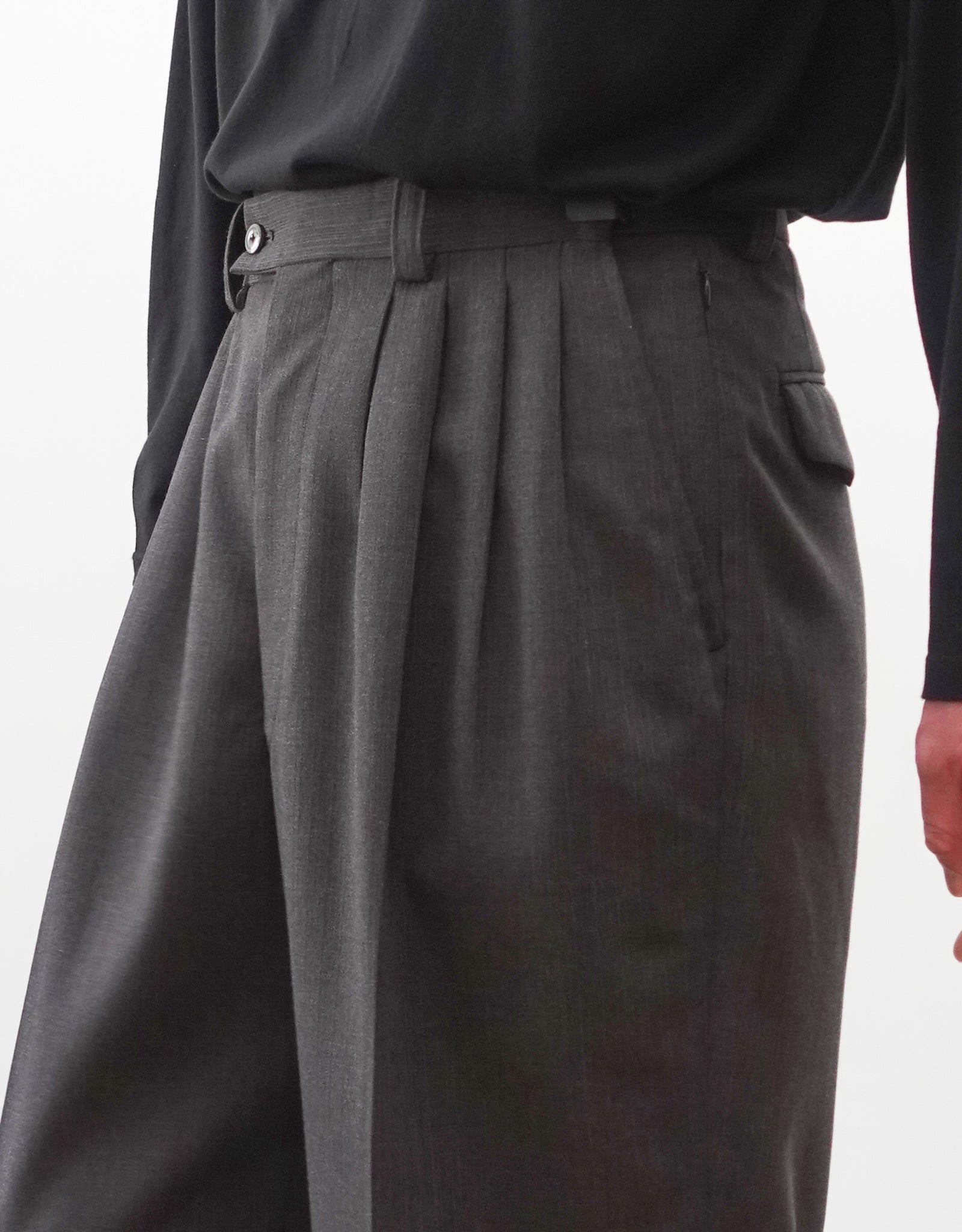 VOUILLON（ヴイヨン）のFour Pleats Wide Trousers - Gray Multi Stripe（4プリーツワイドトラウザーズ）。グレー地にマルチストライプを配した、4プリーツ仕様のワイドパンツ。ストライプによる脚長効果と立体的なシルエットが特徴。モデル着用右向きウエストアップ画像。