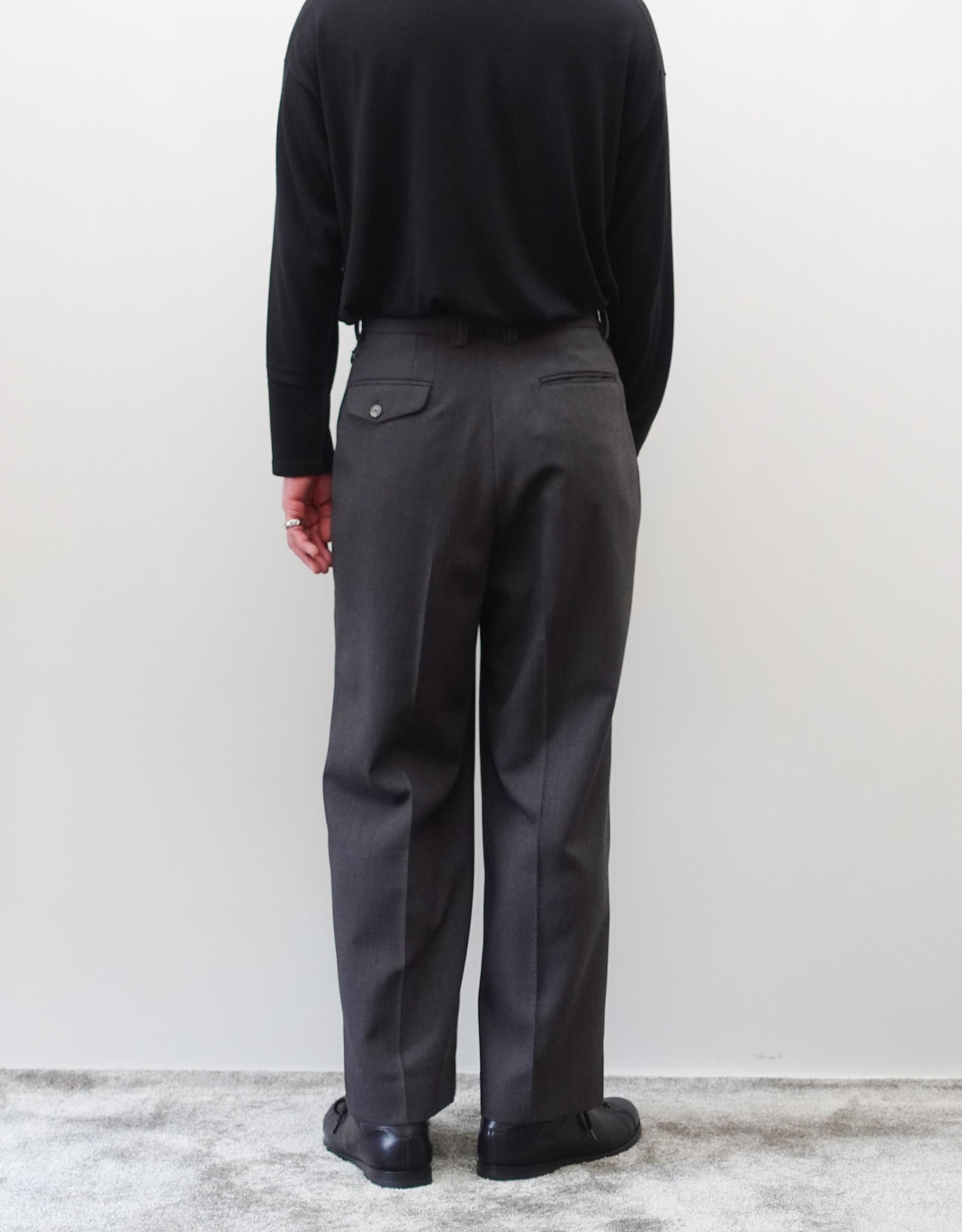 VOUILLON（ヴイヨン）のFour Pleats Wide Trousers - Gray Multi Stripe（4プリーツワイドトラウザーズ）。グレー地にマルチストライプを配した、4プリーツ仕様のワイドパンツ。ストライプによる脚長効果と立体的なシルエットが特徴。モデル着用背面画像。