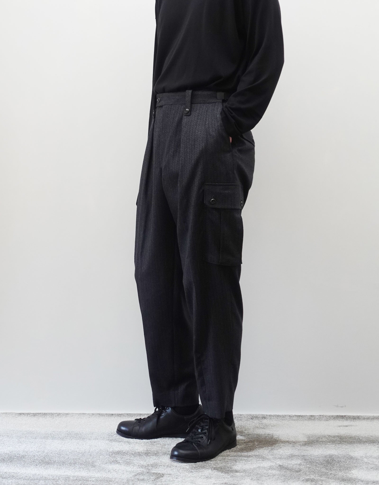 VOUILLON（ヴイヨン）のTwo Tuck Cargo Slacks - chacoal Stripe（2タックカーゴスラックス - チャコールストライプ）。上質な生地で立体的に仕上げることでシルエットの美しさとカーゴポケットの機能性の両立させたカーゴパンツ。モデル着用右斜め前向き画像。