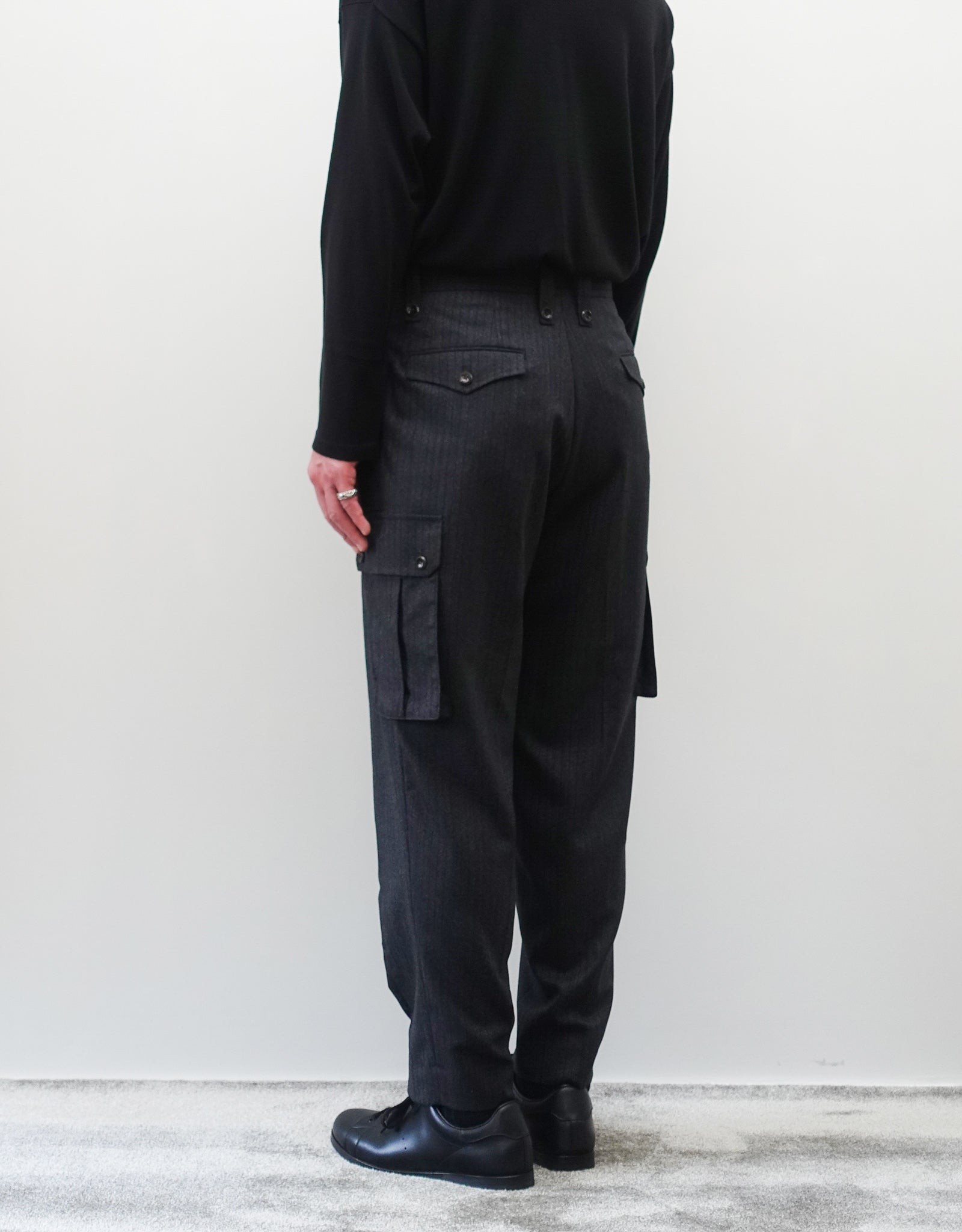 VOUILLON（ヴイヨン）のTwo Tuck Cargo Slacks - chacoal Stripe（2タックカーゴスラックス - チャコールストライプ）。上質な生地で立体的に仕上げることでシルエットの美しさとカーゴポケットの機能性の両立させたカーゴパンツ。モデル着用右斜め後向き画像。