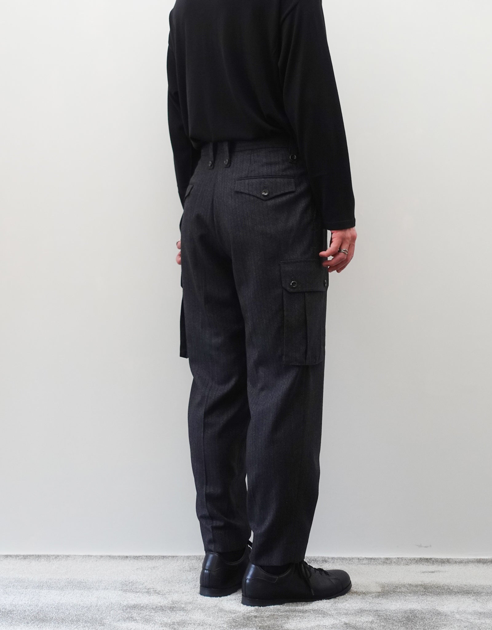 VOUILLON（ヴイヨン）のTwo Tuck Cargo Slacks - chacoal Stripe（2タックカーゴスラックス - チャコールストライプ）。上質な生地で立体的に仕上げることでシルエットの美しさとカーゴポケットの機能性の両立させたカーゴパンツ。モデル着用左斜め後向き画像。