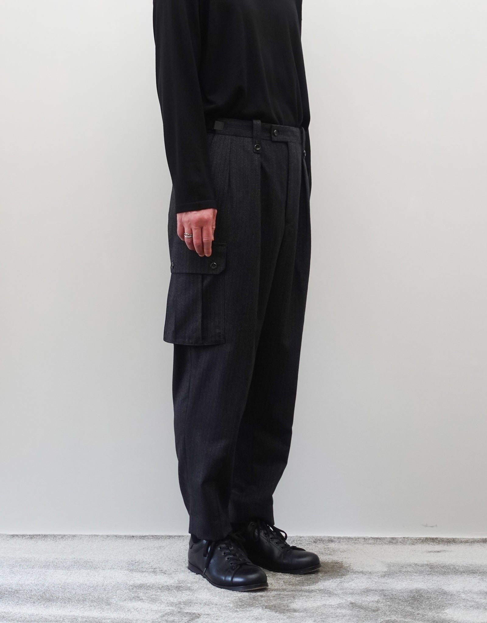 VOUILLON（ヴイヨン）のTwo Tuck Cargo Slacks - chacoal Stripe（2タックカーゴスラックス - チャコールストライプ）。上質な生地で立体的に仕上げることでシルエットの美しさとカーゴポケットの機能性の両立させたカーゴパンツ。モデル着用左斜め前向き画像。