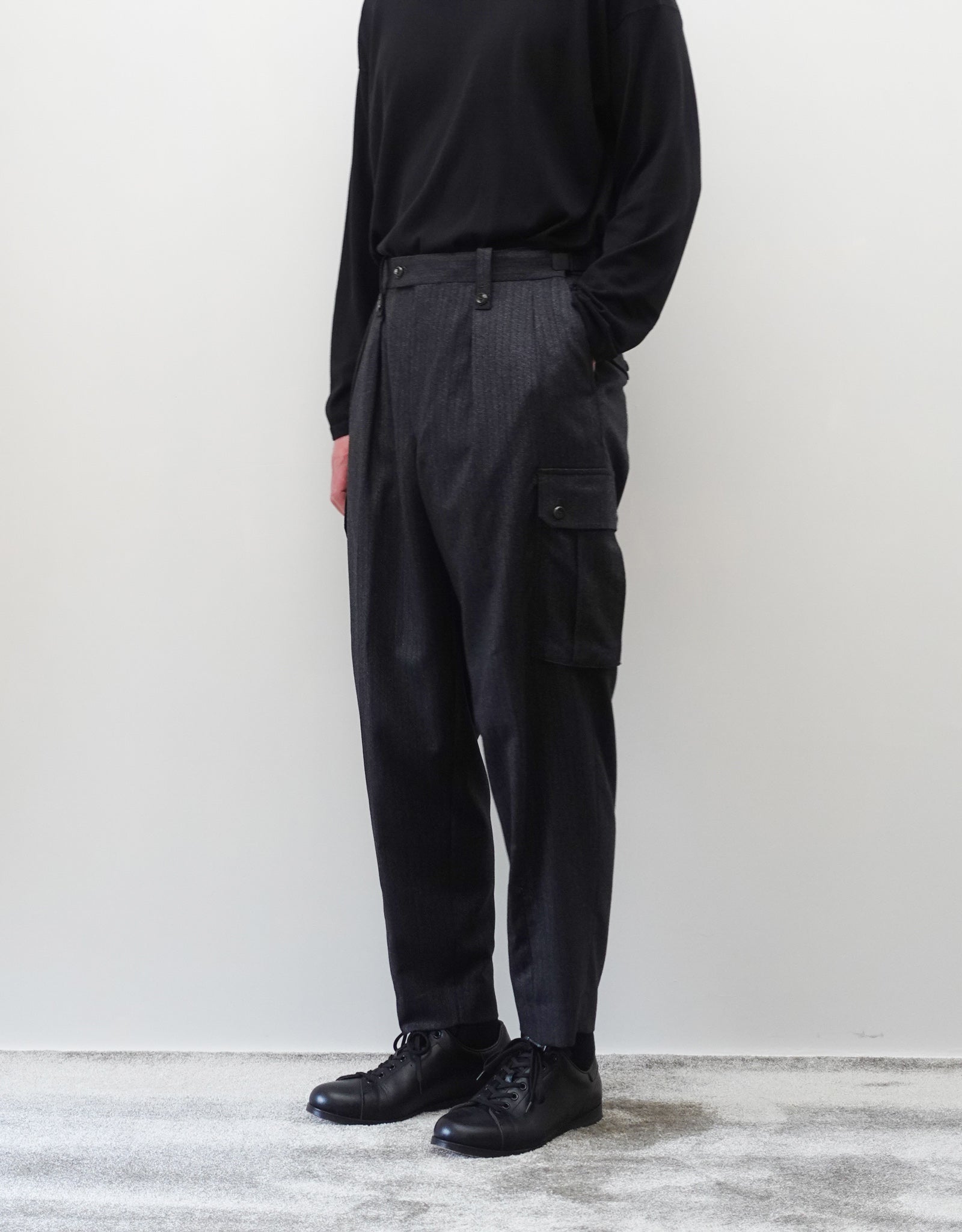 VOUILLON（ヴイヨン）のTwo Tuck Cargo Slacks - chacoal Stripe（2タックカーゴスラックス - チャコールストライプ）。上質な生地で立体的に仕上げることでシルエットの美しさとカーゴポケットの機能性の両立させたカーゴパンツ。モデル着用左ポケットに手を入れている正面画像。