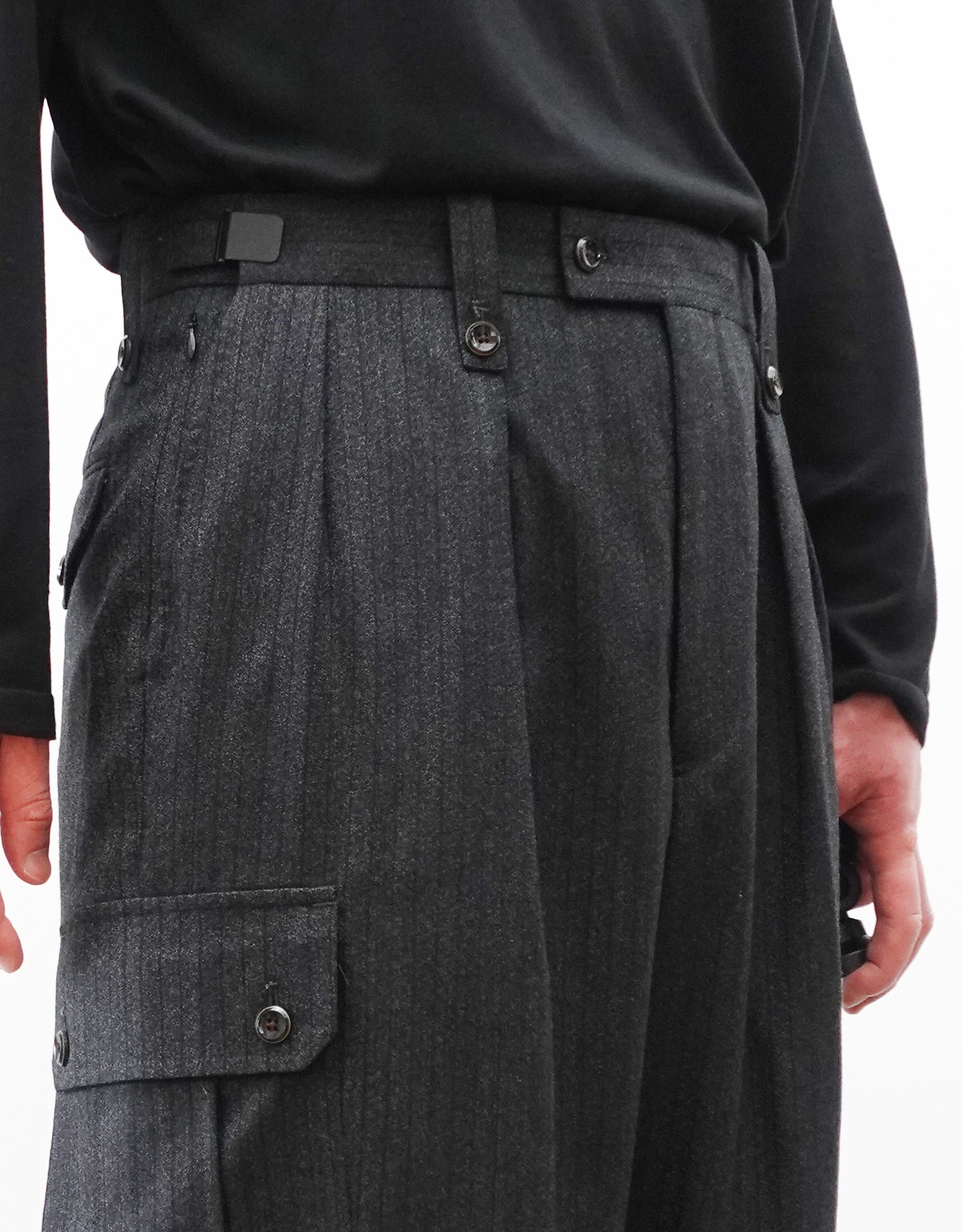 VOUILLON（ヴイヨン）のTwo Tuck Cargo Slacks - chacoal Stripe（2タックカーゴスラックス - チャコールストライプ）。上質な生地で立体的に仕上げることでシルエットの美しさとカーゴポケットの機能性の両立させたカーゴパンツ。モデル着用左斜め前向きウエストアップ画像。
