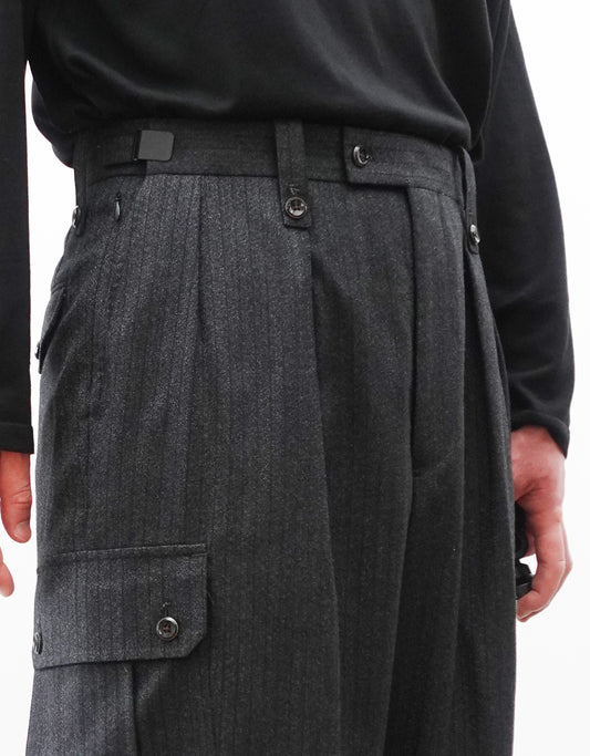 VOUILLON（ヴイヨン）のTwo Tuck Cargo Slacks - chacoal Stripe（2タックカーゴスラックス - チャコールストライプ）。上質な生地で立体的に仕上げることでシルエットの美しさとカーゴポケットの機能性の両立させたカーゴパンツ。モデル着用左斜め前向きウエストアップ画像。