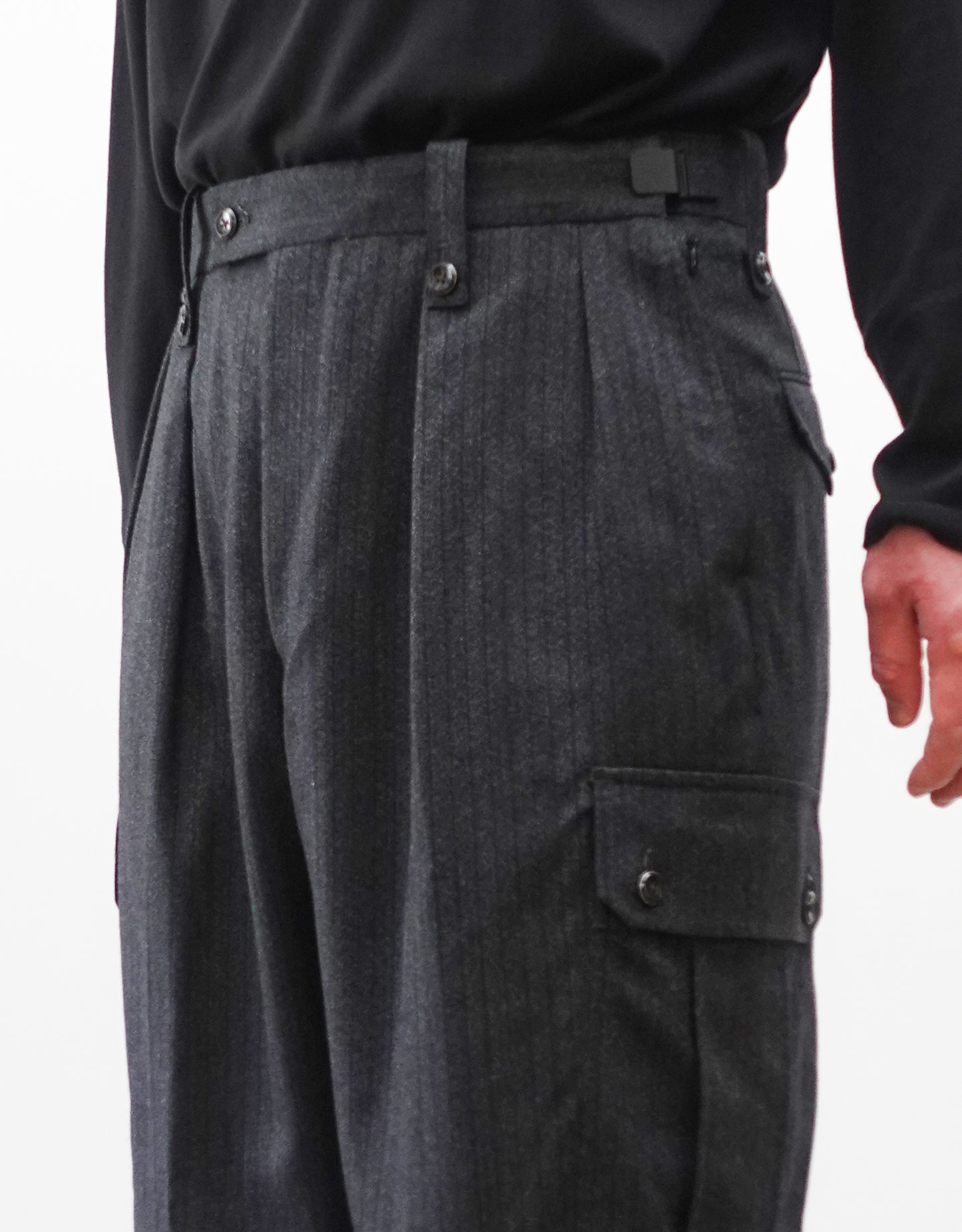 VOUILLON（ヴイヨン）のTwo Tuck Cargo Slacks - chacoal Stripe（2タックカーゴスラックス - チャコールストライプ）。上質な生地で立体的に仕上げることでシルエットの美しさとカーゴポケットの機能性の両立させたカーゴパンツ。モデル着用右斜め前向きウエストアップ画像。