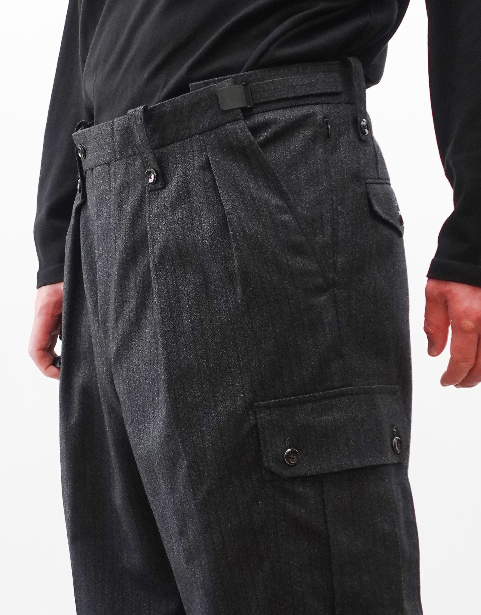 VOUILLON（ヴイヨン）のTwo Tuck Cargo Slacks - chacoal Stripe（2タックカーゴスラックス - チャコールストライプ）。上質な生地で立体的に仕上げることでシルエットの美しさとカーゴポケットの機能性の両立させたカーゴパンツ。モデル着用右斜め前向きウエストアップのアジャスター最大開き画像。