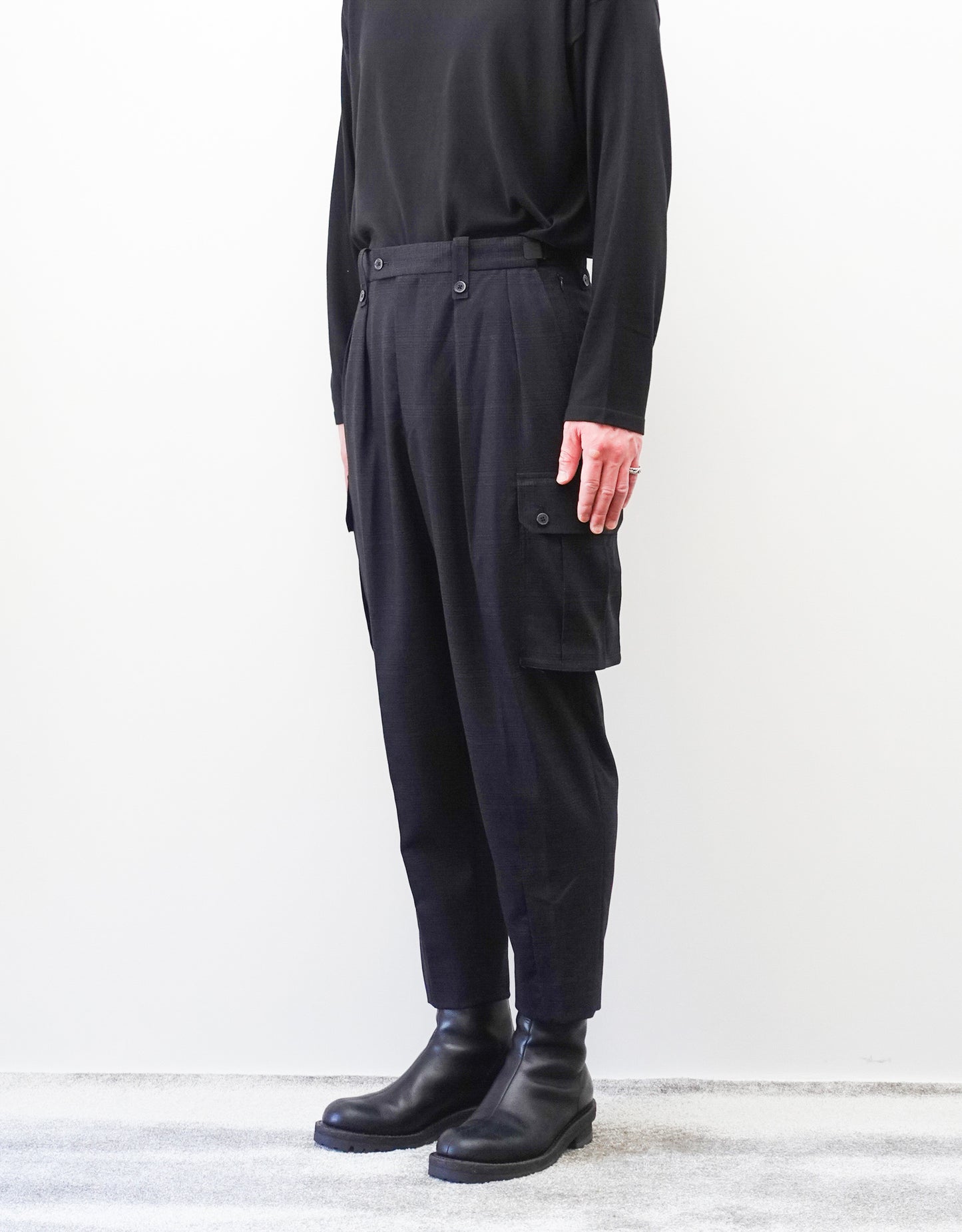 VOUILLON（ヴイヨン）のTwo Tuck Cargo Slacks - Black Glen Check（ツータックカーゴスラックス）。黒を基調としたシックなグレンチェック柄生地に、腰元のツータックと上品なサイドポケットを配したモードなカーゴパンツ。モデル着用右斜め前向き画像。