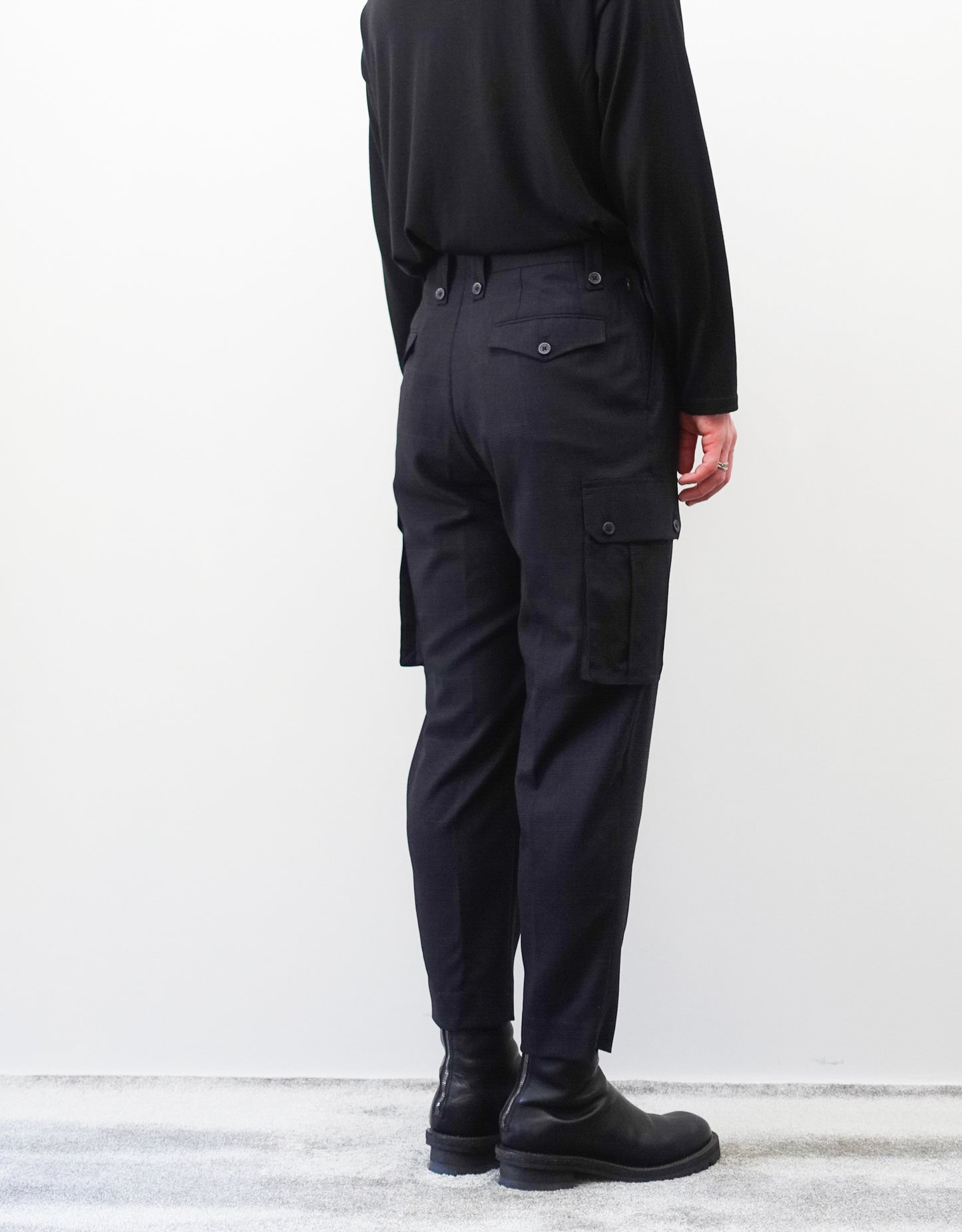 VOUILLON（ヴイヨン）のTwo Tuck Cargo Slacks - Black Glen Check（ツータックカーゴスラックス）。黒を基調としたシックなグレンチェック柄生地に、腰元のツータックと上品なサイドポケットを配したモードなカーゴパンツ。モデル着用左後向き画像。