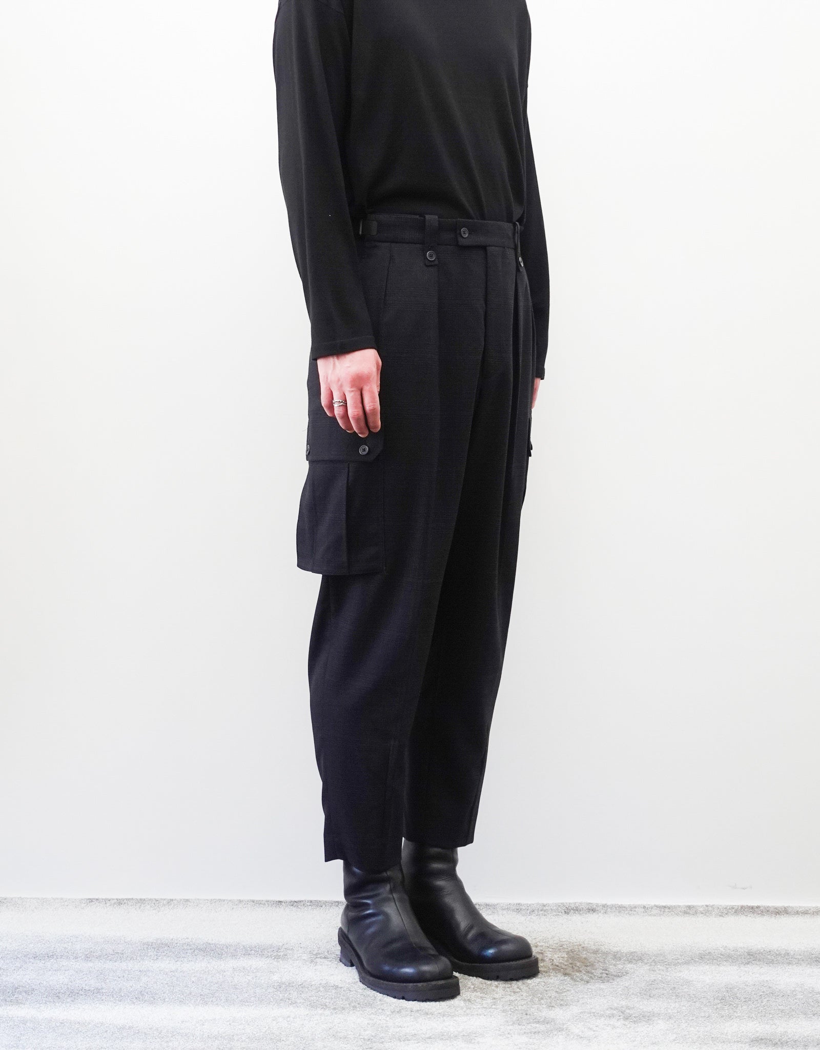 VOUILLON（ヴイヨン）のTwo Tuck Cargo Slacks - Black Glen Check（ツータックカーゴスラックス）。黒を基調としたシックなグレンチェック柄生地に、腰元のツータックと上品なサイドポケットを配したモードなカーゴパンツ。モデル着用左斜め前向き画像。