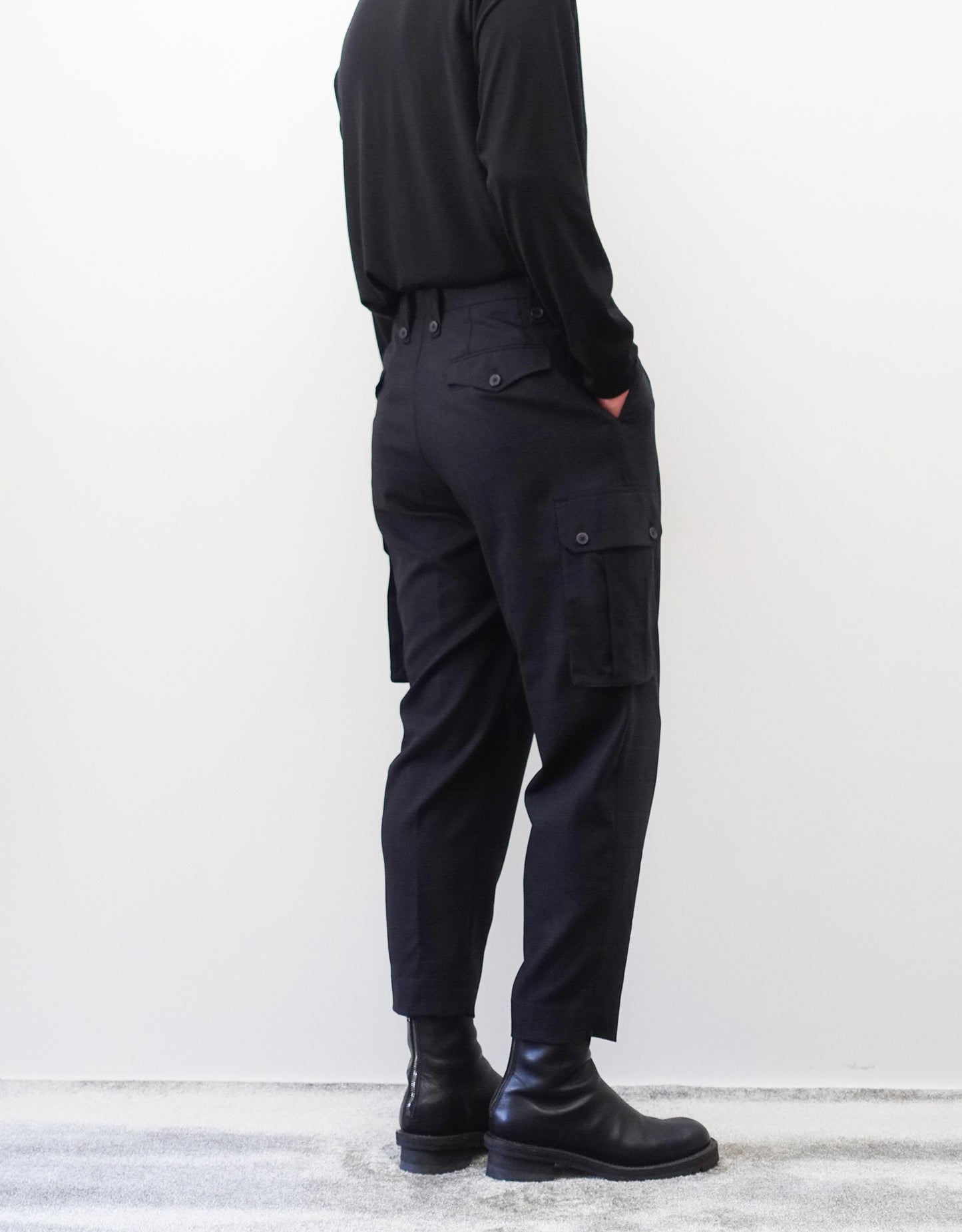 VOUILLON（ヴイヨン）のTwo Tuck Cargo Slacks - Black Glen Check（ツータックカーゴスラックス）。黒を基調としたシックなグレンチェック柄生地に、腰元のツータックと上品なサイドポケットを配したモードなカーゴパンツ。モデル着用左向き画像。